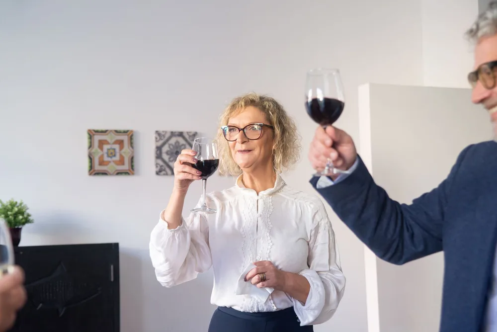 Elderly friends celebrating indoors with glasses of red wine, enjoying a cheerful gathering