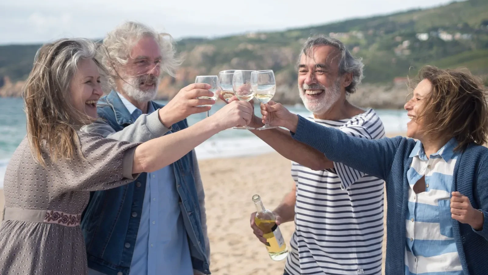 Elderly friends celebrating with wine on a sunny Portuguese beach, embracing happiness and togetherness