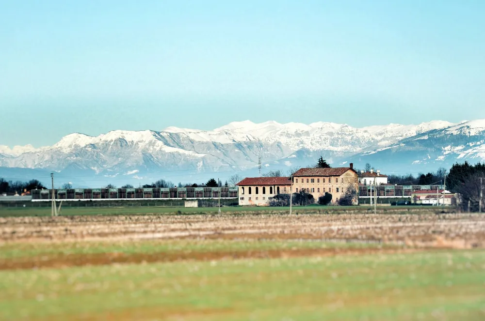 Farmhouse in rural setting with mountains and fields, under a clear sky