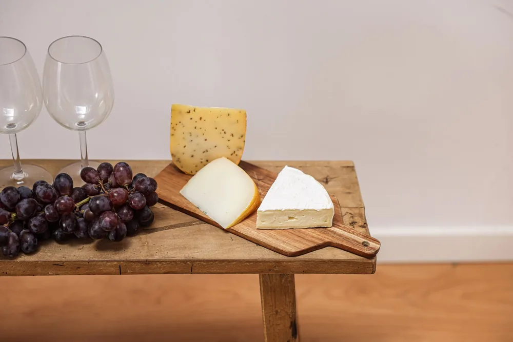 Featuring gourmet cheeses, grapes, and wine glasses on a rustic wooden board
