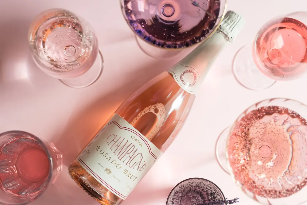 Flat lay of rosé champagne bottle with various glasses on a light pink background