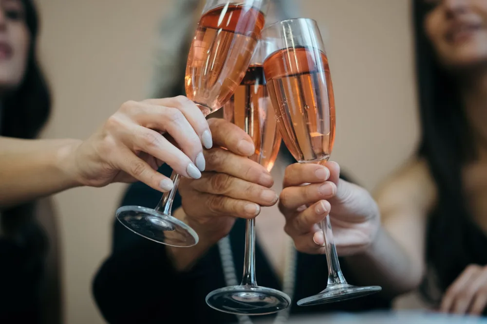Four hands toasting with rosé wine glasses in a festive indoor setting