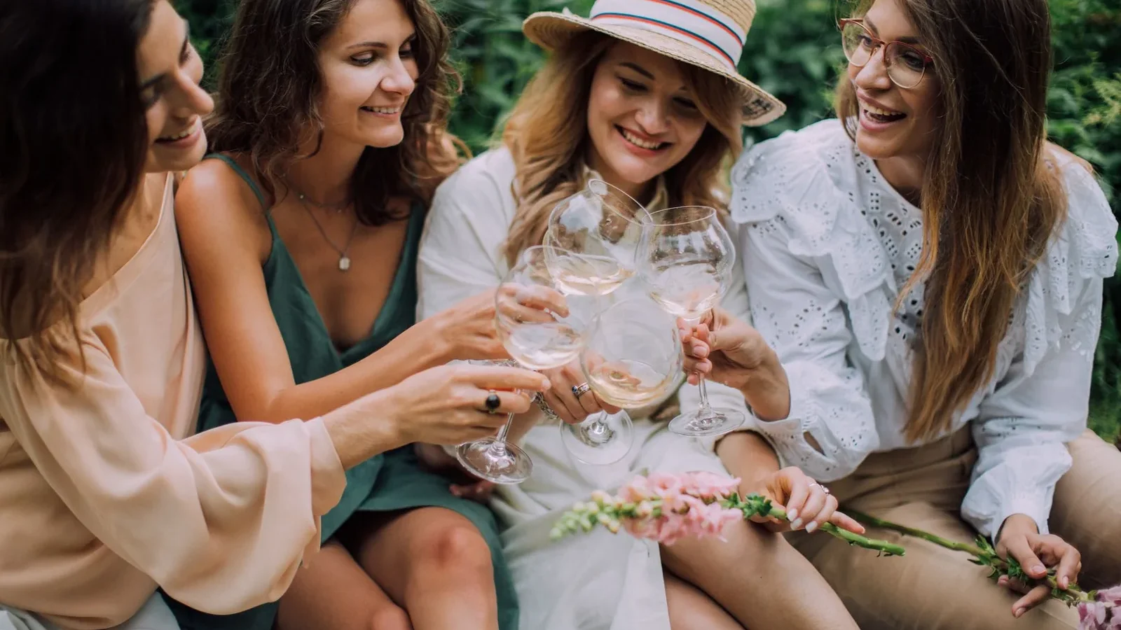 Four women celebrating with white wine outdoors, smiling and enjoying a summer day