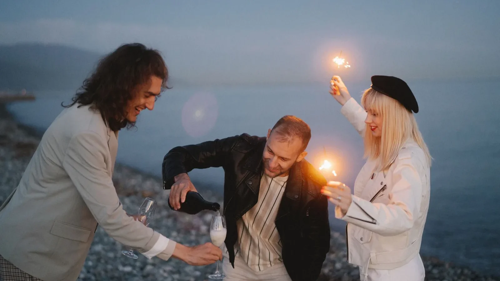 Friends celebrating by the beach with champagne and sparklers, enjoying a festive evening outdoors