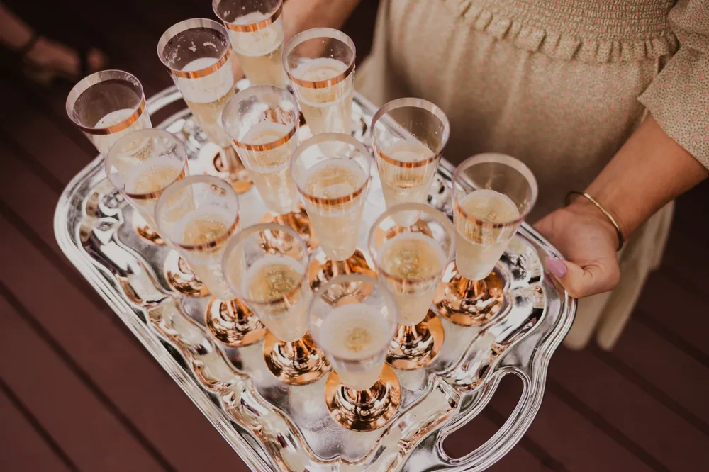 From above of crop female holding tray with glasses of champagne in daylight