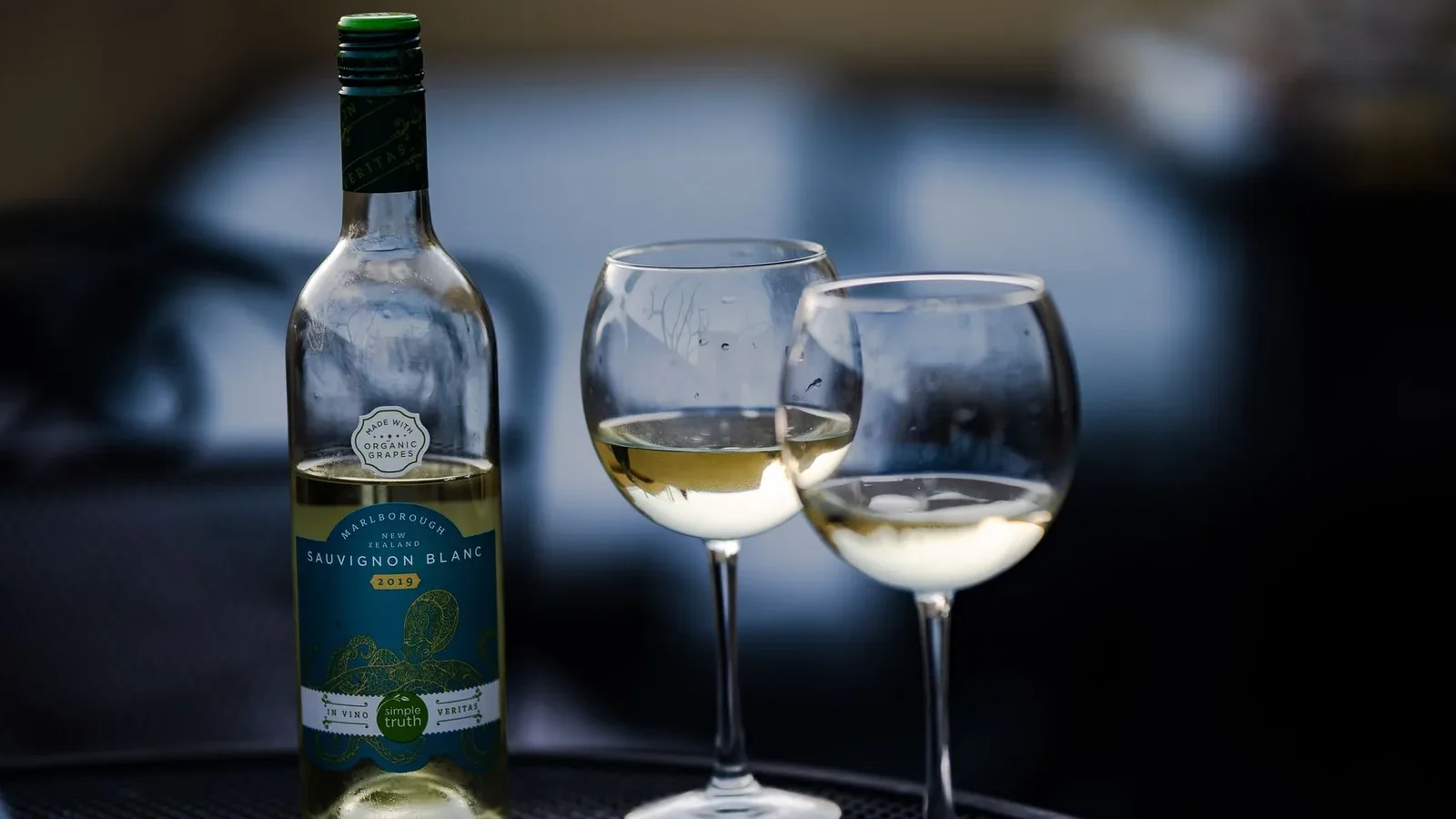 Glass bottle of wine placed near crystal wineglasses on round table in cafe