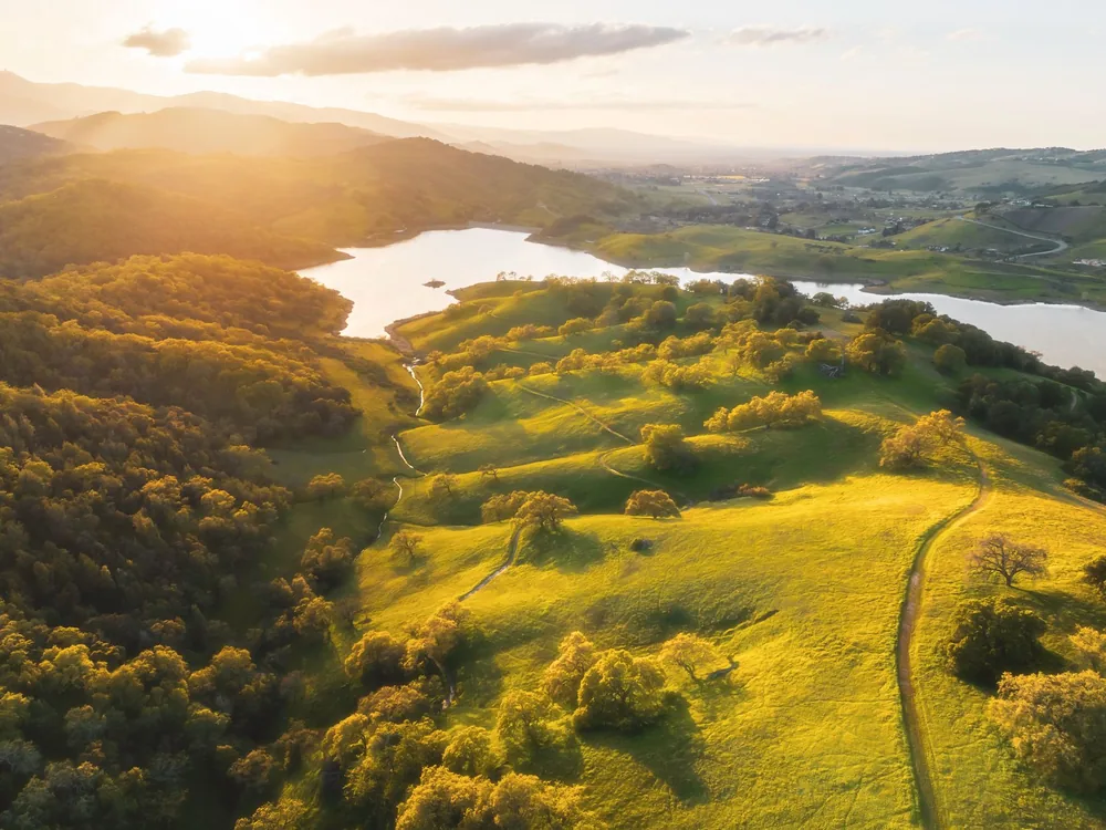 Golden hour aerial view of rolling hills and lake in San Jose, California
