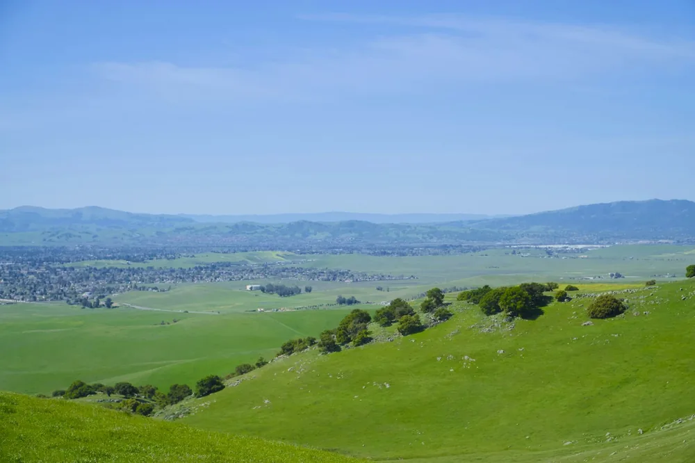 Green hills meet the distant mountains under a blue sky
