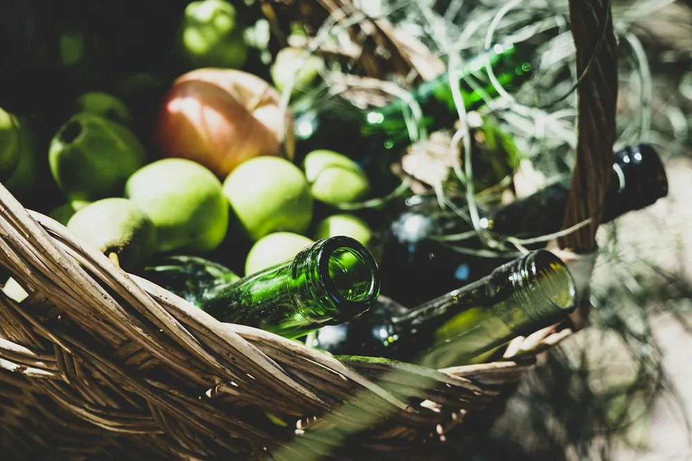 Green mango fruits near empty bottles on brown wicker basket