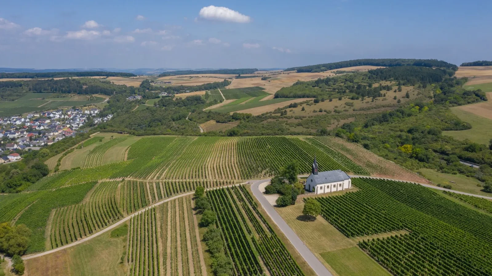 Green plantations with furrows and rows with crops located against cloudy sky in rural terrain near settlement