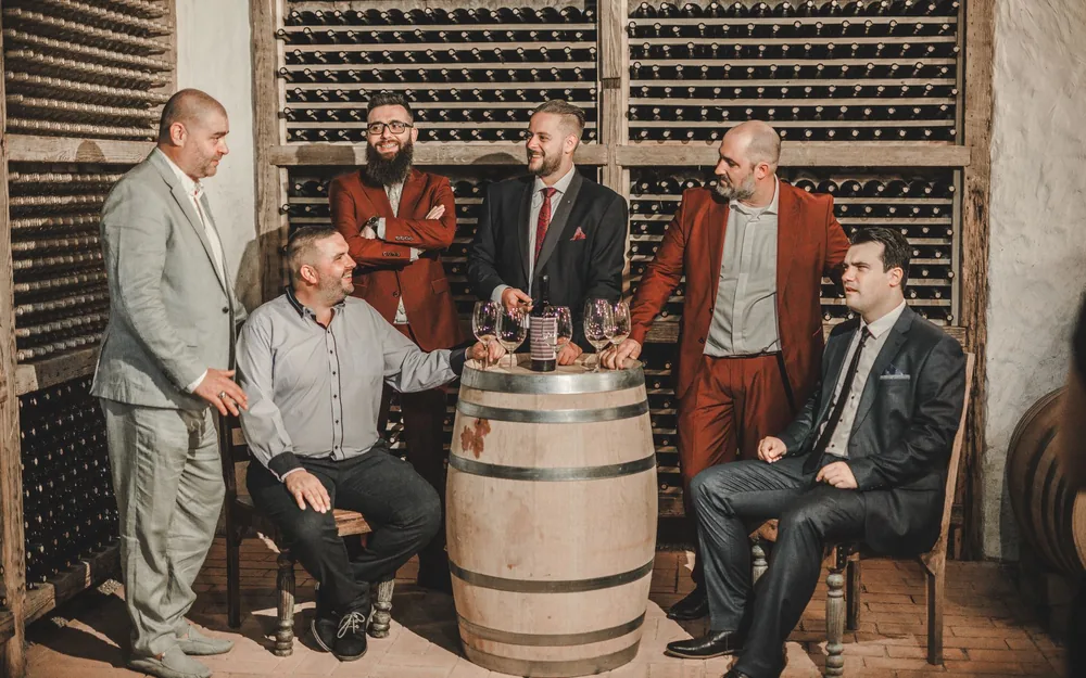 Group of adults in suits enjoying wine in a cozy cellar setting with oak barrels and wine racks