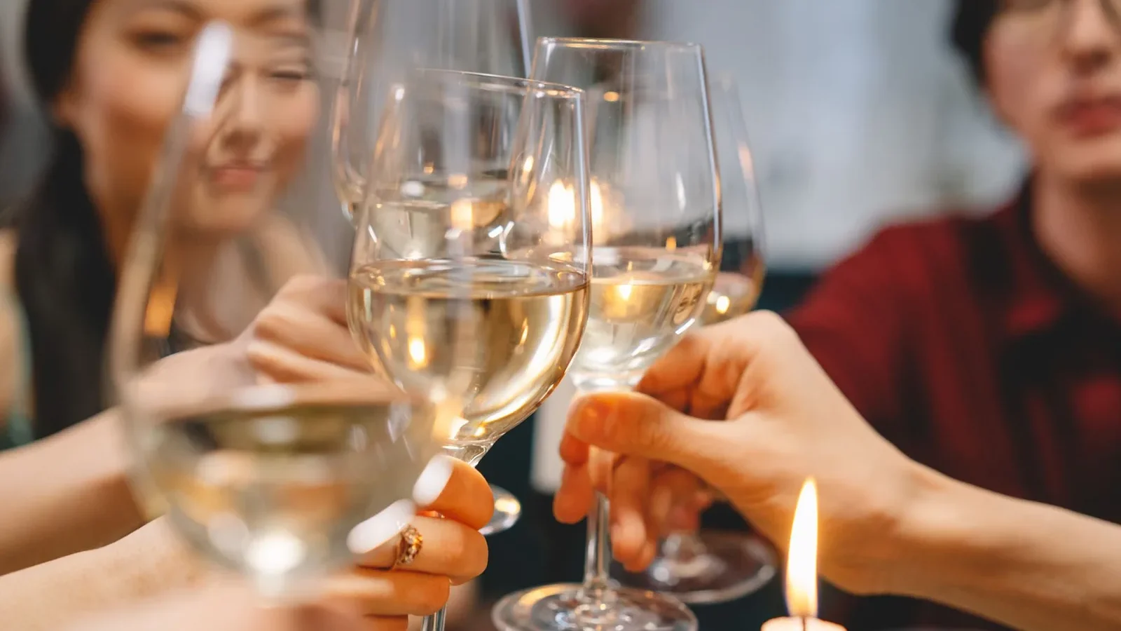 Group of friends toasting with white wine glasses indoor, creating a warm and festive atmosphere