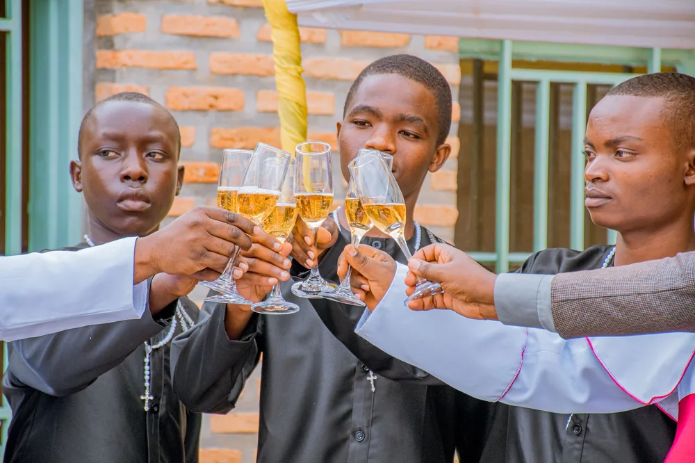Group of young men clinking champagne glasses in celebration, wearing religious attire outdoors