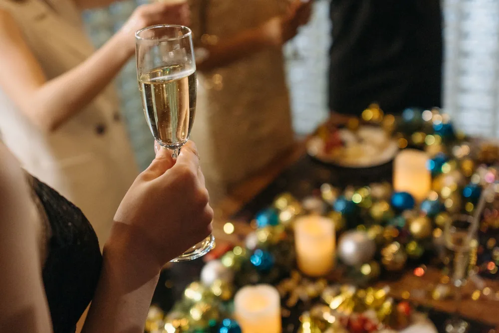 Hands holding champagne glasses at a festive gathering with candles and decor