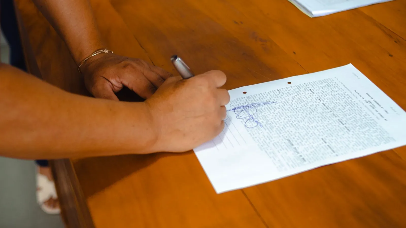 Hands signing a legal document on a wooden table indoors