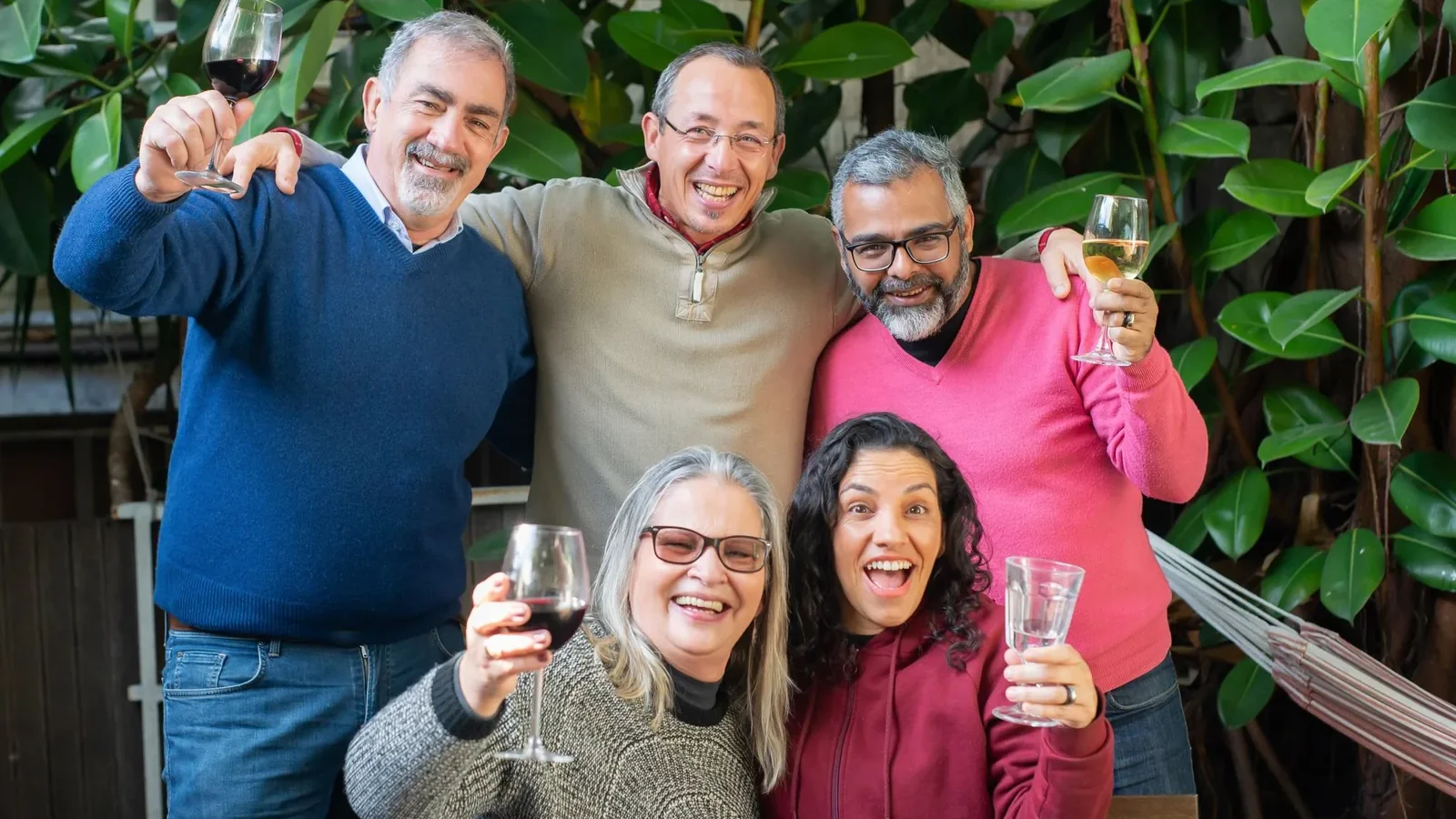Happy group of friends smiling and toasting with wine in a lush outdoor setting