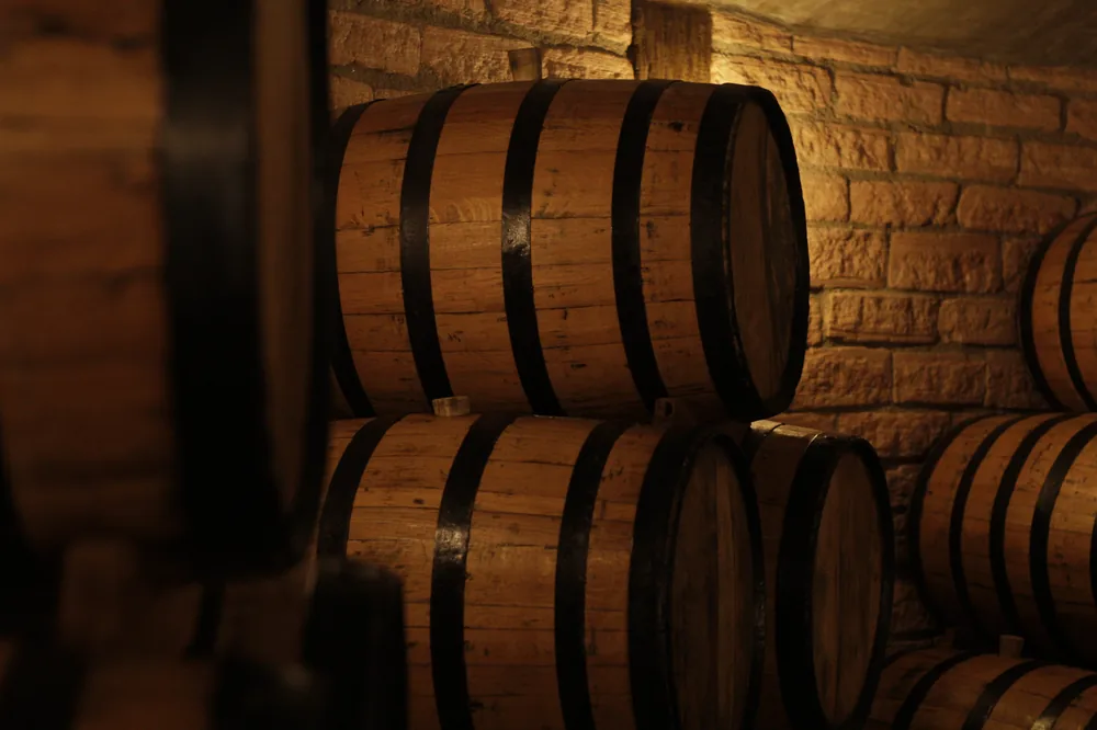 Heap of wooden barrels arranged together in underground wine cellar with warm light