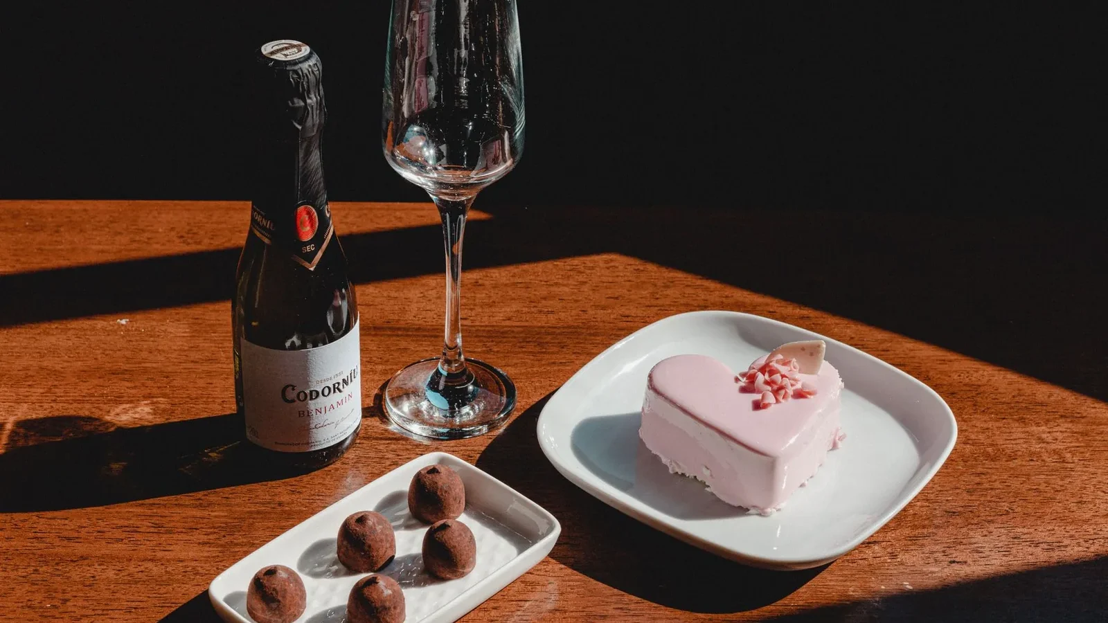 Heart-shaped cake and chocolates with champagne on a wooden table, ideal for celebrations