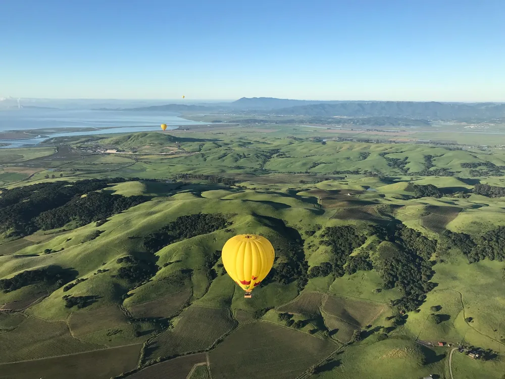Hot air balloons floating above lush Californian hills under a clear blue sky
