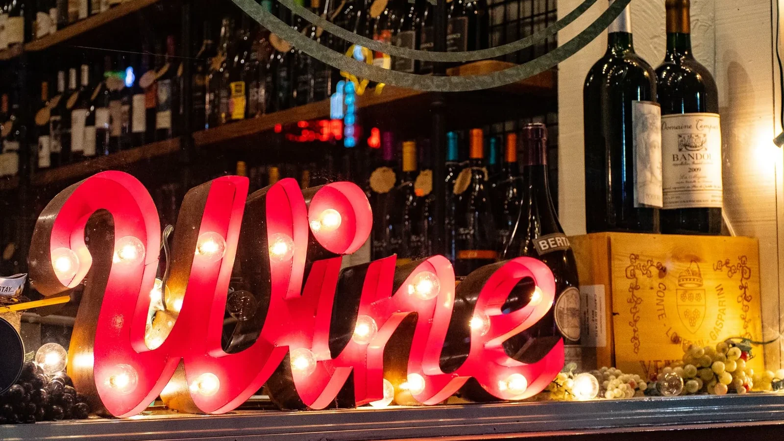 Illuminated wine sign with bottles and grapes create a lively ambiance in a liquor store window