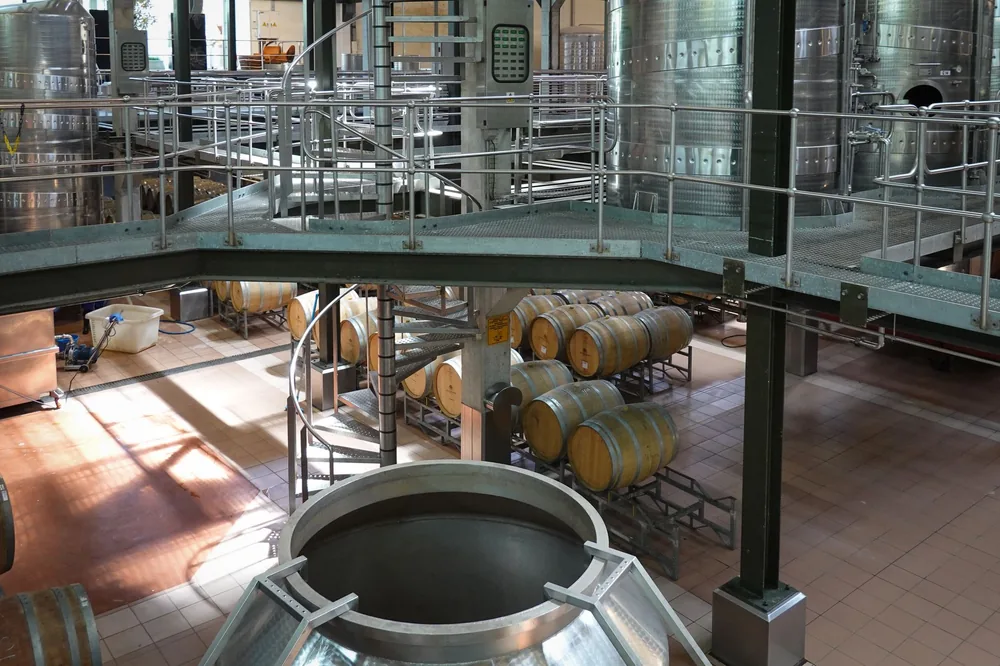 Interior view of a modern wine cellar featuring wooden barrels and large steel fermentation tanks