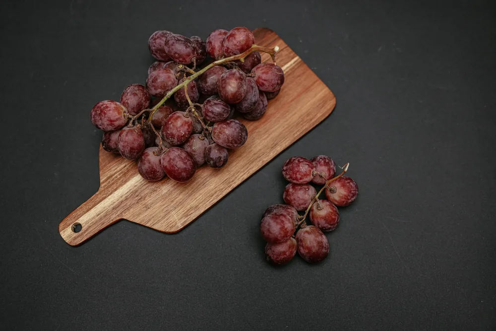 Juicy red grapes displayed elegantly on a wooden board with a black background, perfect for culinary themes