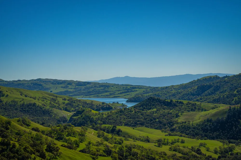 Landscape of Sunol, California with rolling hills and a reservoir under a clear blue sky