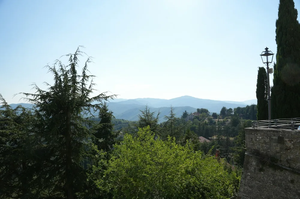 Landscape with distant mountains, green trees, and an old lamppost