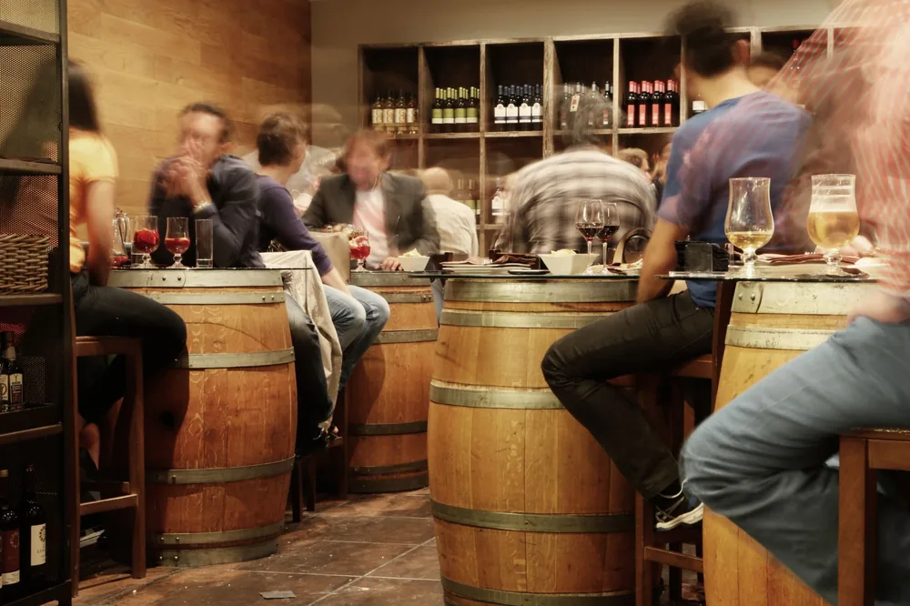 Lively bar setting with people enjoying drinks and tapas around wine barrel tables