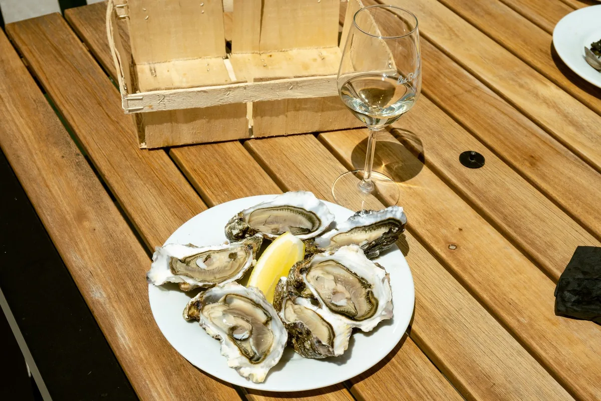A glass of pale white wine on a wooden table beside a plate of shellfish
