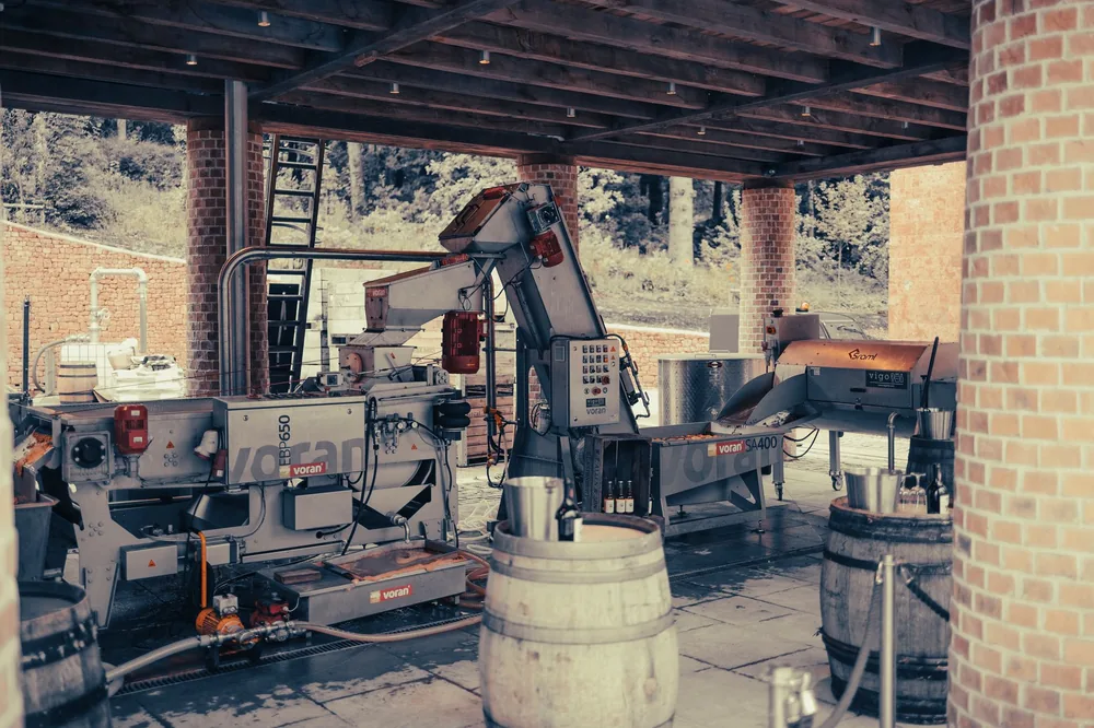 Machinery setup in a vineyard's outdoor shelter with barrels, used in wine production