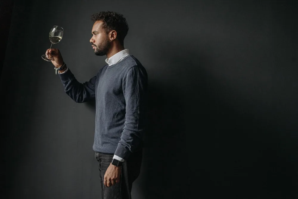 Man in knitwear holding a glass of wine in a studio environment