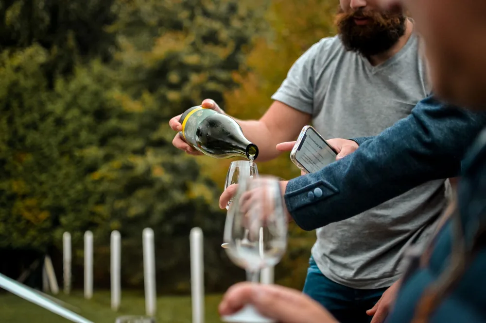 Men enjoying an outdoor gathering, pouring wine into glasses in a lush green setting