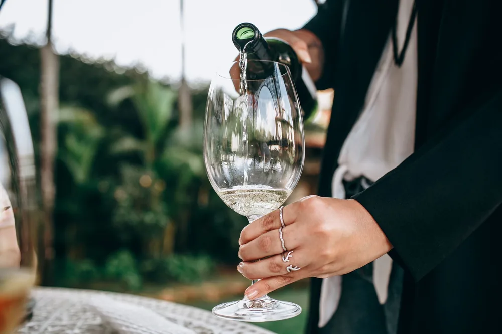 Moment of pouring white wine into a glass set in a lush outdoor garden