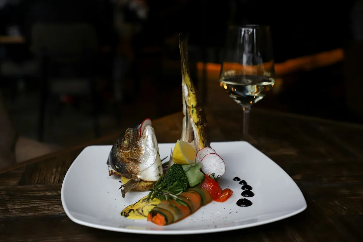 Glass of white wine beside a plate of grilled fish and lemon on an outdoor table