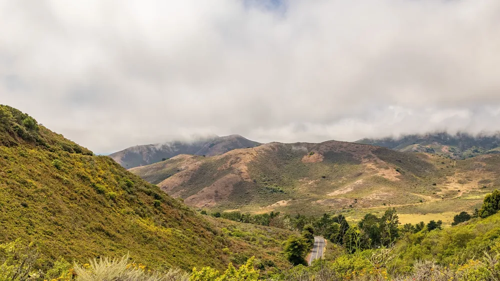 Mountain view with a winding road and clouds overhead, showcasing natural beauty