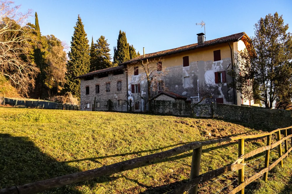 Old farmhouse in scenic countryside, surrounded by trees and a wooden fence