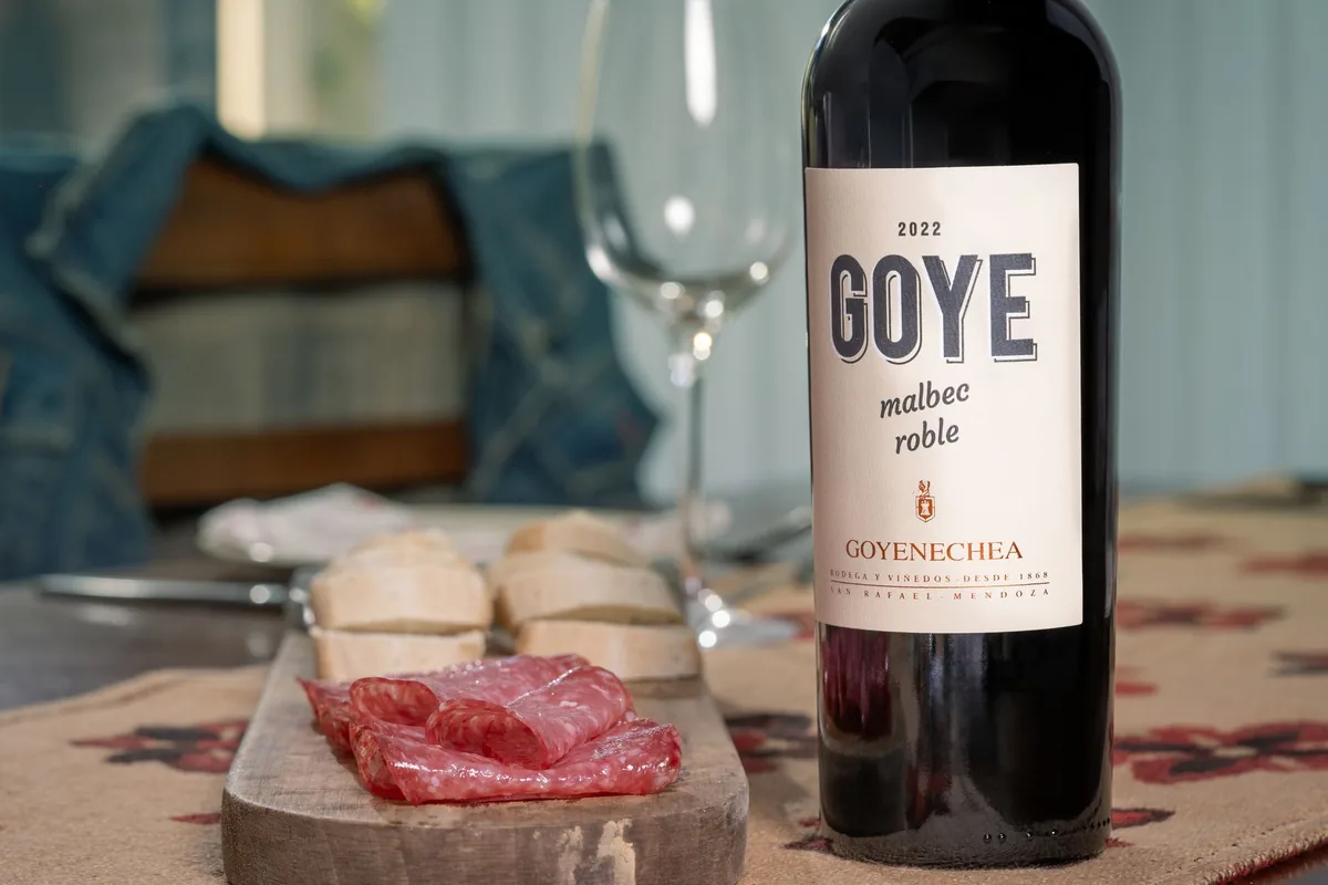 A glass of red wine on an outdoor table beside grilled lamb and herbs
