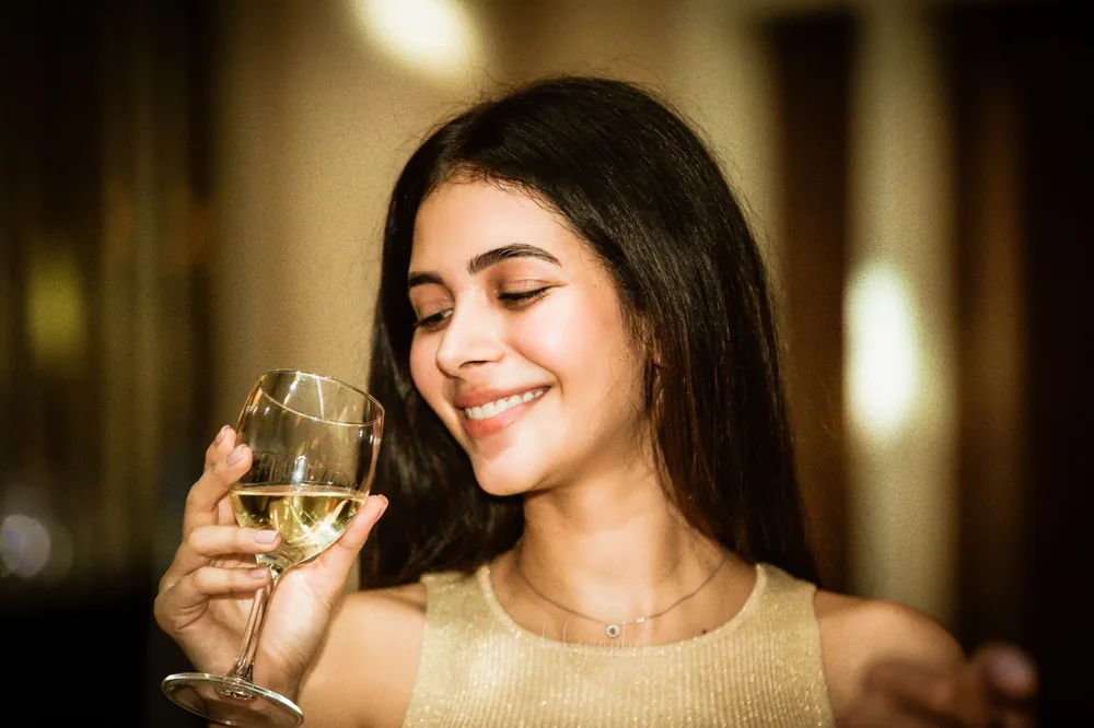 Portrait of a smiling woman enjoying a glass of white wine indoors, creating a joyful and relaxed atmosphere