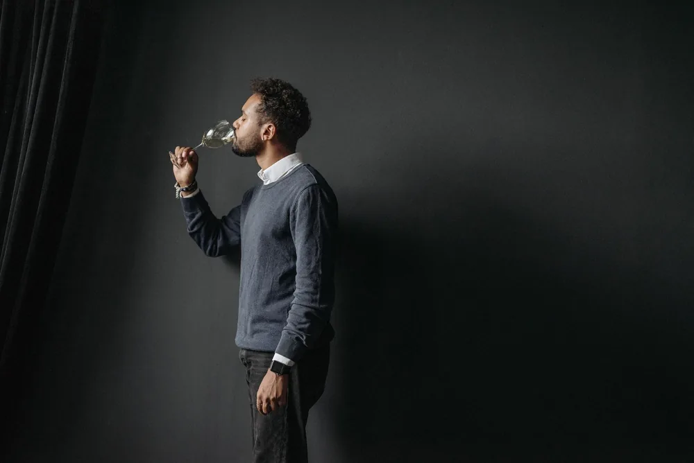 Profile of a man tasting white wine against a dark background, highlighting elegance