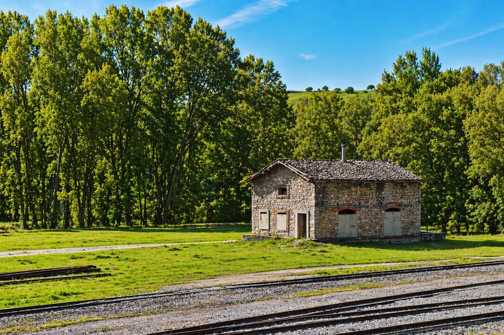 Quaint stone house beside railway in lush green landscape, under summer sky
