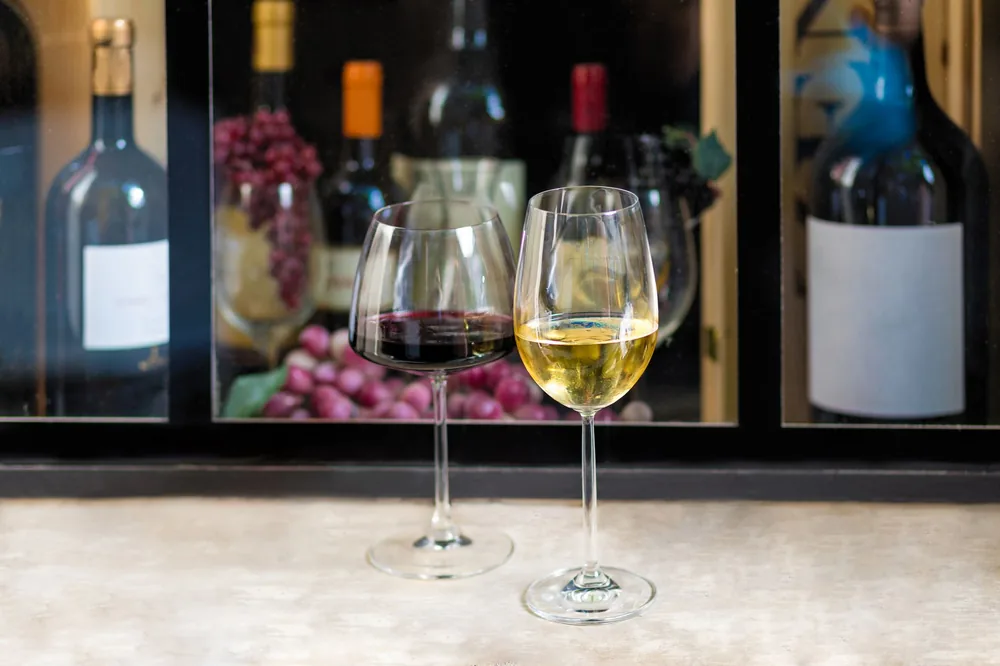 Red and white wine glasses with bottles and grapes in the background, perfect for wine tasting themes