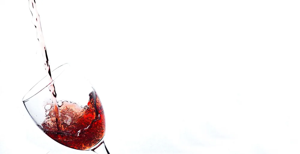Red wine being poured into a tilted glass against a white background. Perfect for beverage and lifestyle themes