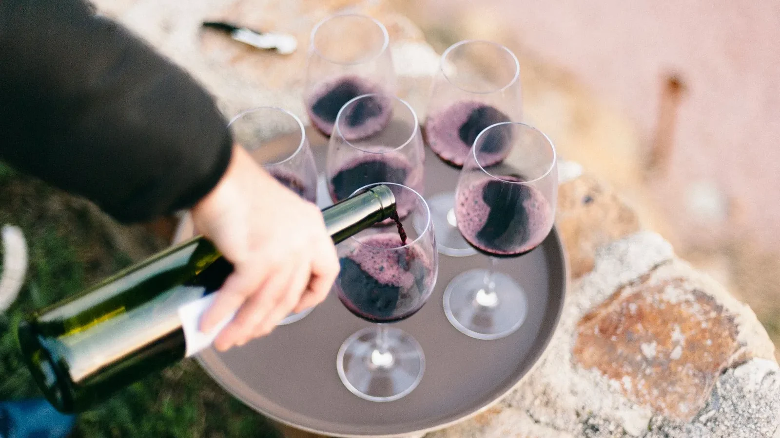 Red wine being poured into glasses on a tray, set outdoors