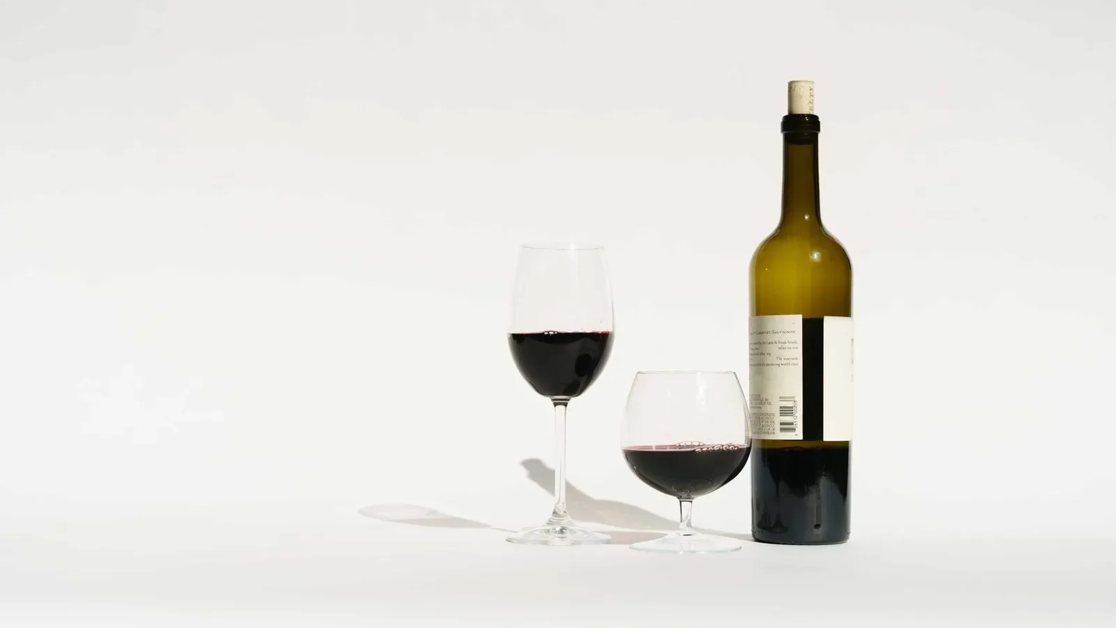 Red wine made from dark colored grape varieties in bottle and glasses placed in white studio
