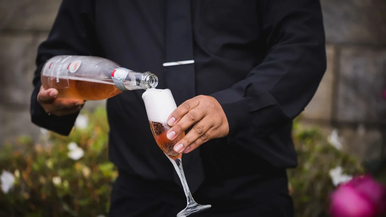 Rosé champagne being poured into a flute by a person in formal attire outdoors