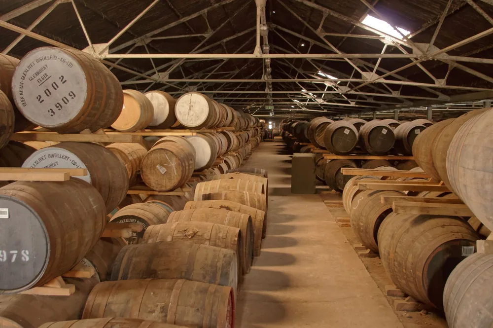 Rows of wooden barrels aging in a historic distillery warehouse, creating a rustic atmosphere