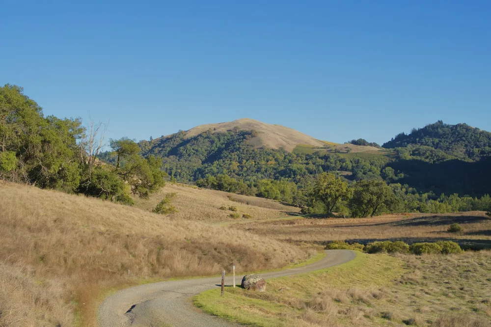 Rural road winds through dry grassy hills towards mountains