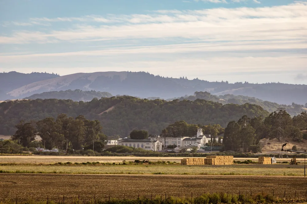 Rural scene featuring haystacks, farmland, and distant hills under a blue sky