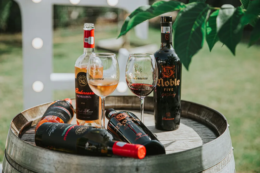 Rustic display of bottled wines and glasses on a wooden barrel in an outdoor setting